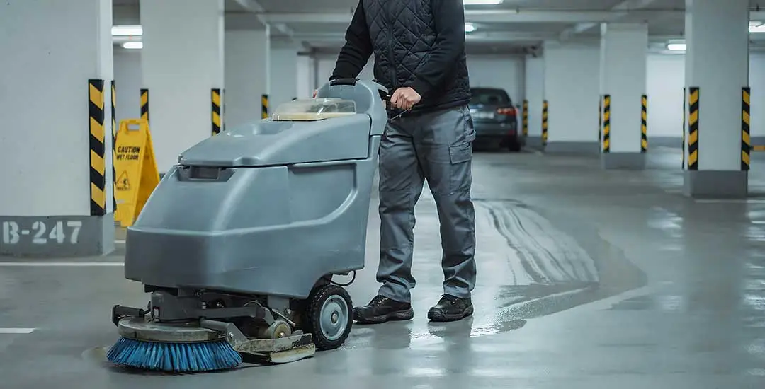 Operario con barredora industrial durante la limpieza y mantenimiento de garajes